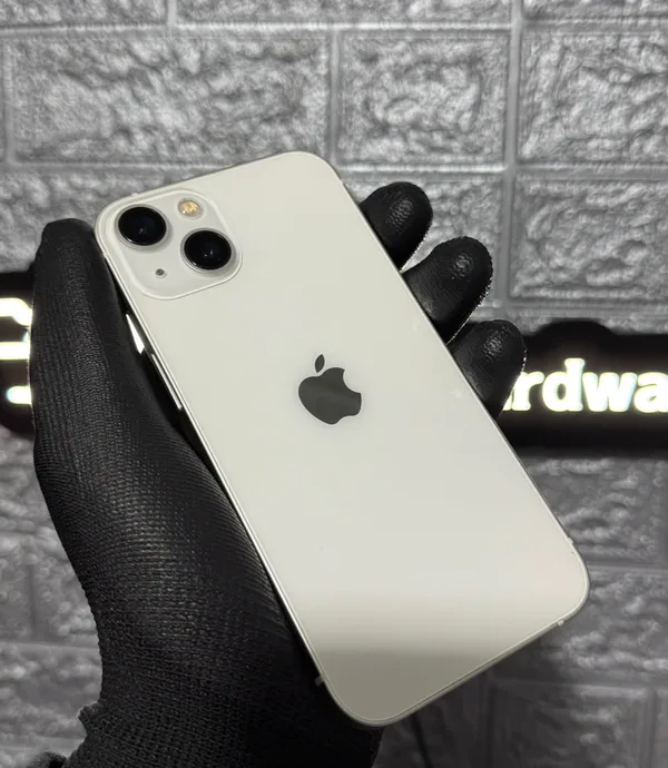 iPhone 13 branco segurado com luva preta em frente ao letreiro da loja