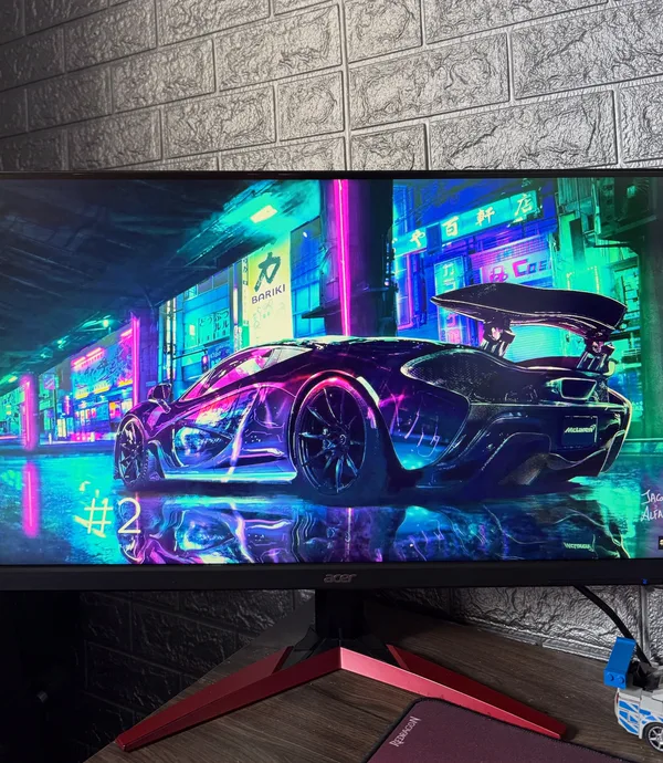 Monitor gamer ligado mostrando um carro neon, com a parede da loja ao fundo